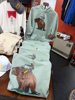 Collection of hoodies and t-shirts with bear graphics on a table against a red wall.